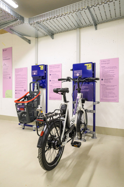 Nahaufnahme der E-Ladestation in einer Mobilitätsstation. Daneben hängt ein Schild mit Erläuterungen zur Ausleihe von E-Lastenfahrrädern.