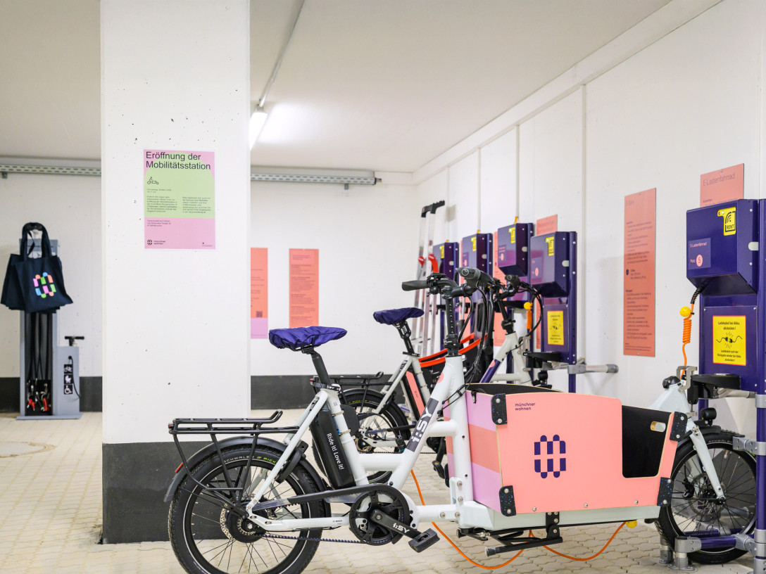 Blick in eine Mobilitätsstation. Mehrere Lastenräder mit Münchner Wohnen Logo hängen an E-Ladestationen.
