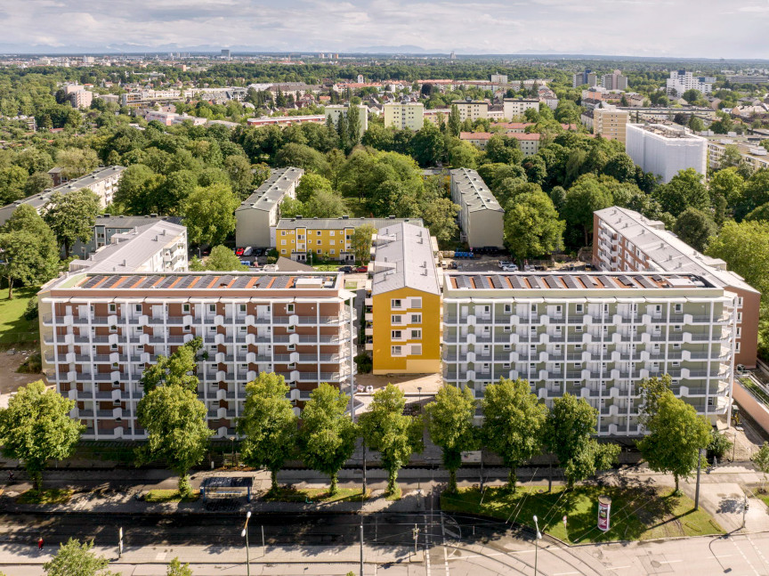 Drohnenaufnahme der Neubauten entlang der Zschokkestraße. Der mehrstöckige Gebäuderiegel ist u-förmig, in der Mitte sieht man eine etwas niedrigere Gebäudezeile. Drumherum sehr viel grüner Baumbestand.