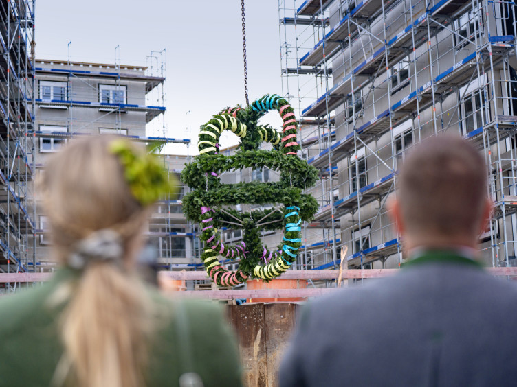 Ein Pärchen in bayerischer Tracht schaut auf eine Baustelle und eine Richtkrone.