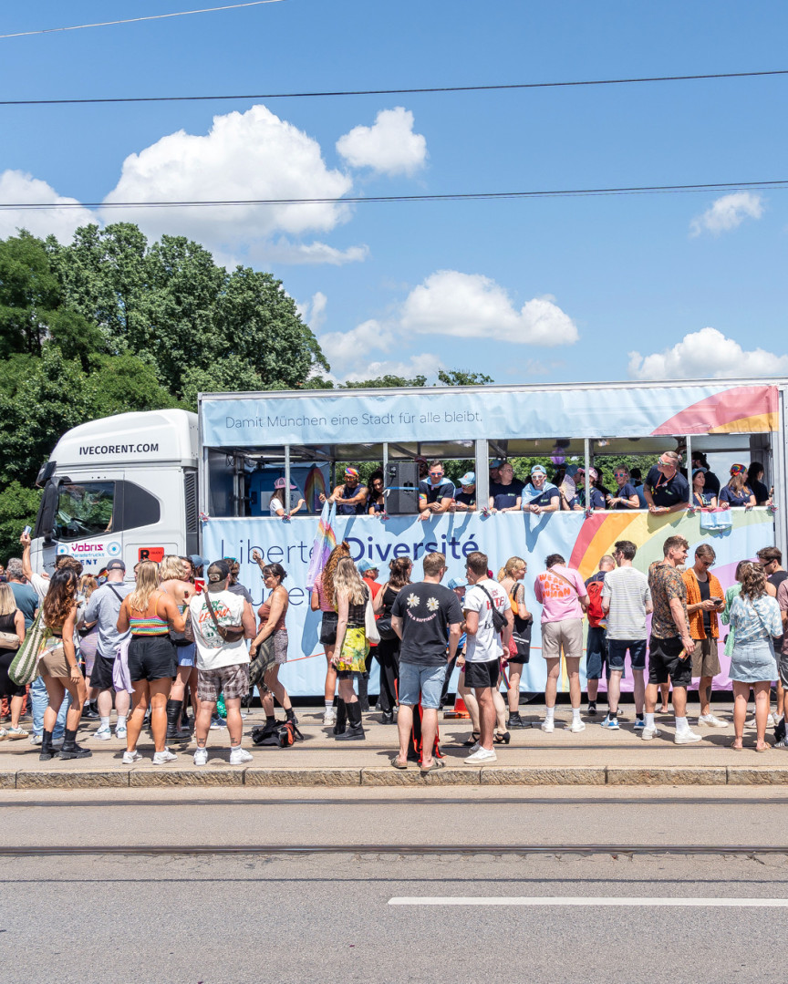 Truck der Münchner Wohnen auf einer Brücke der über die Isar. Hunderte feiernde Menschen stehen davor.