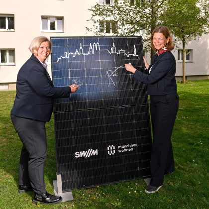 Zwei Frauen stehen im Innenhof einer Wohnanlage. Zwischen ihnen halten sie ein Solarpanel und unterschreiben darauf.