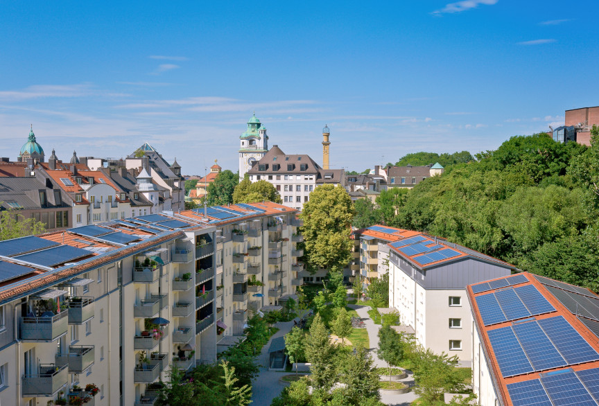 Blick über eine Wohnanlage mit Photovoltaikanlage auf dem Dach. Im Hintergrund ist ein Wohnhaus und ein Kirchturm zu erkennen.