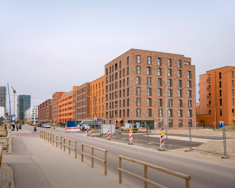 Ansicht eines Wohnhauses mit Backsteinfassade. Drumherum erkennt man weitere Neubauten.